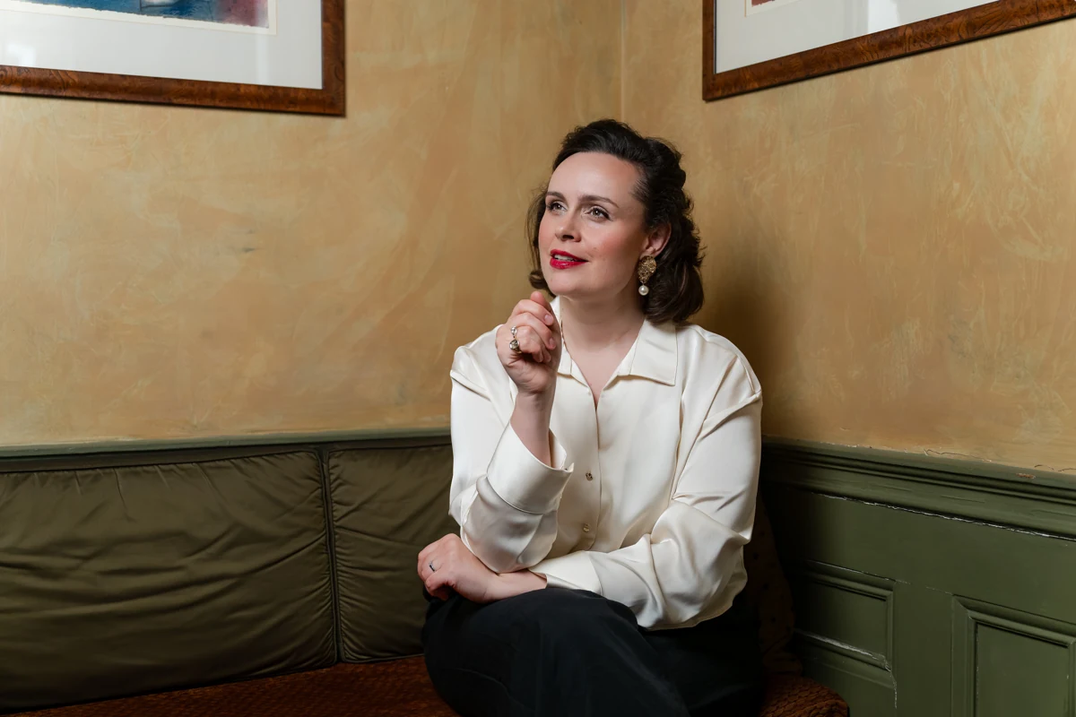 Katy Thomson seated in a white blouse, resting her chin on her hand