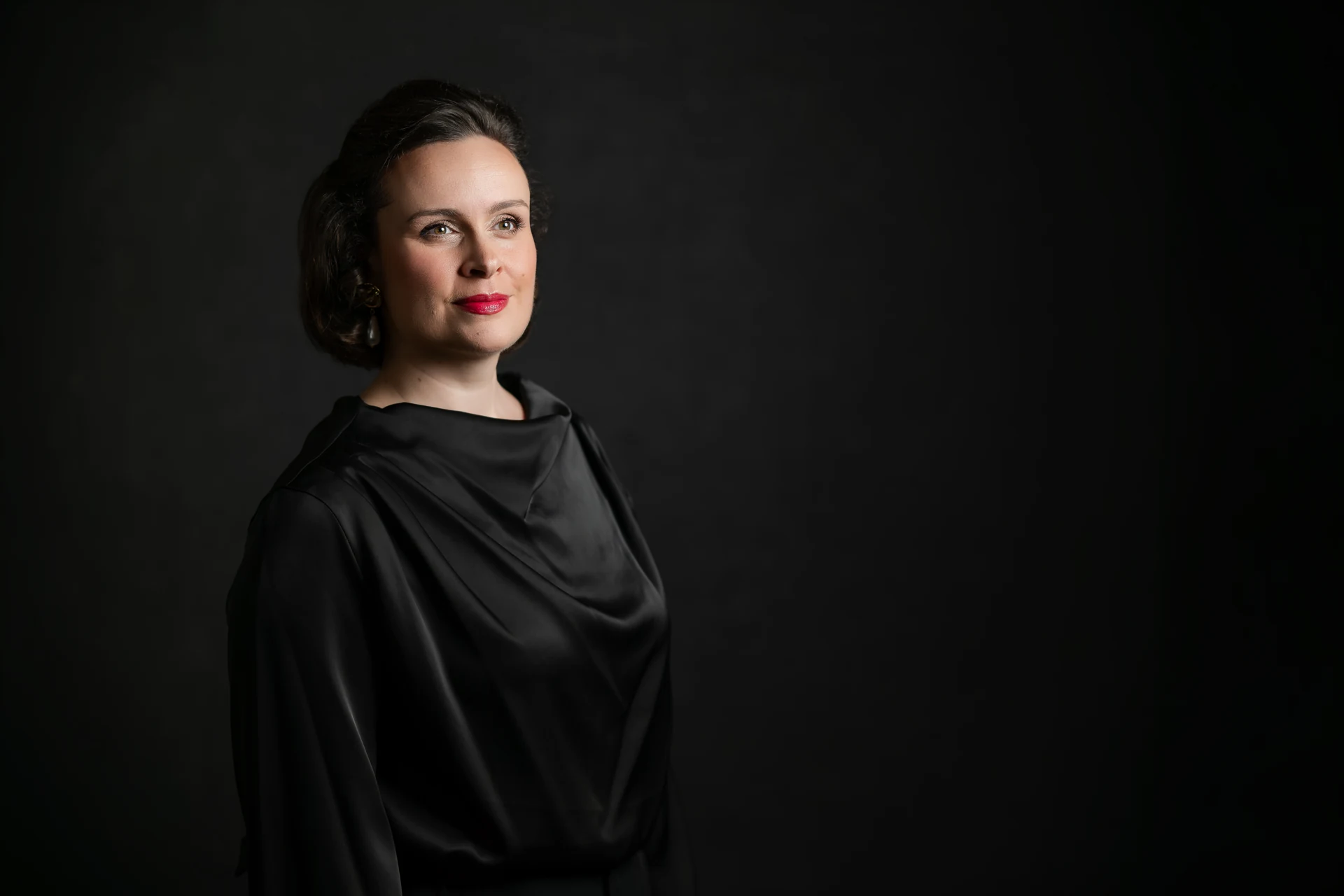 Katy Thomson in a sculptural black draped outfit, looking to the right