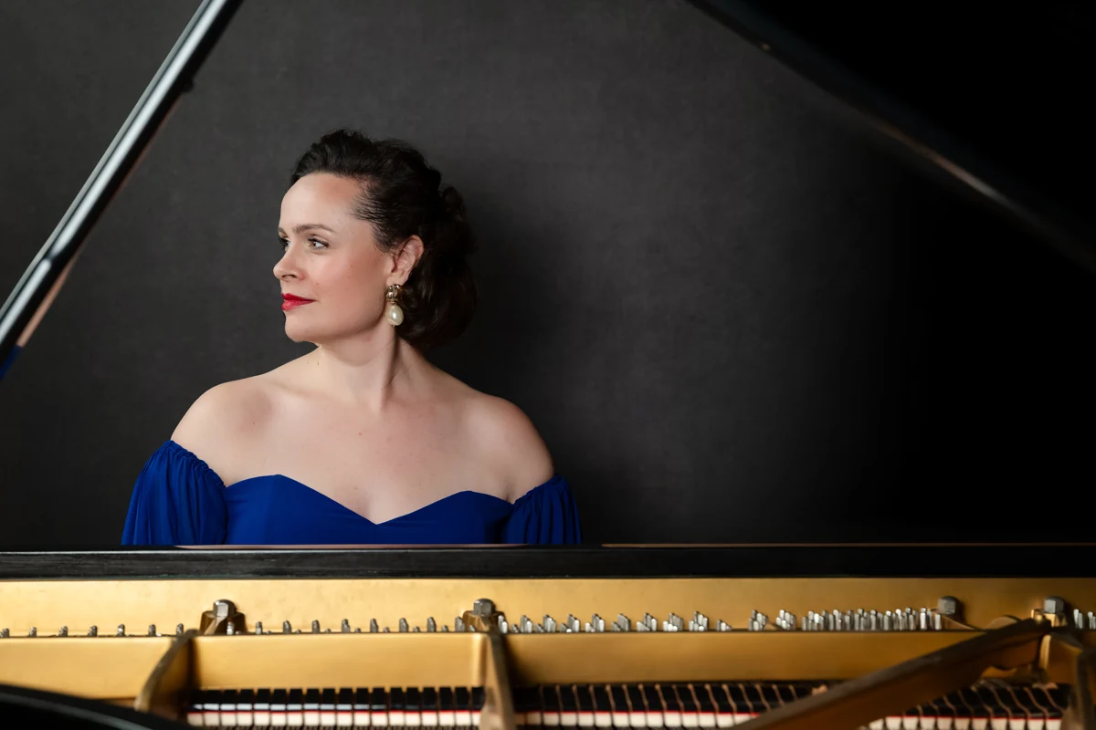 Katy Thomson in a cobalt blue gown behind an open grand piano
