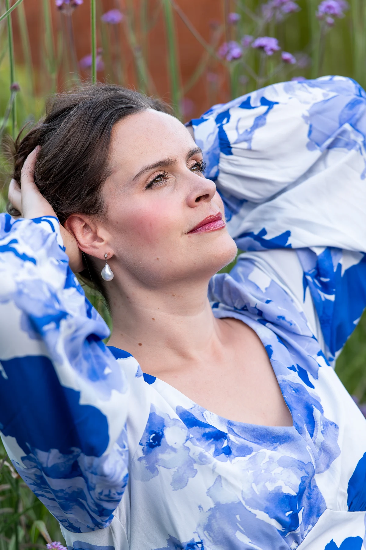 Katy Thomson wearing a blue floral dress among pink garden flowers