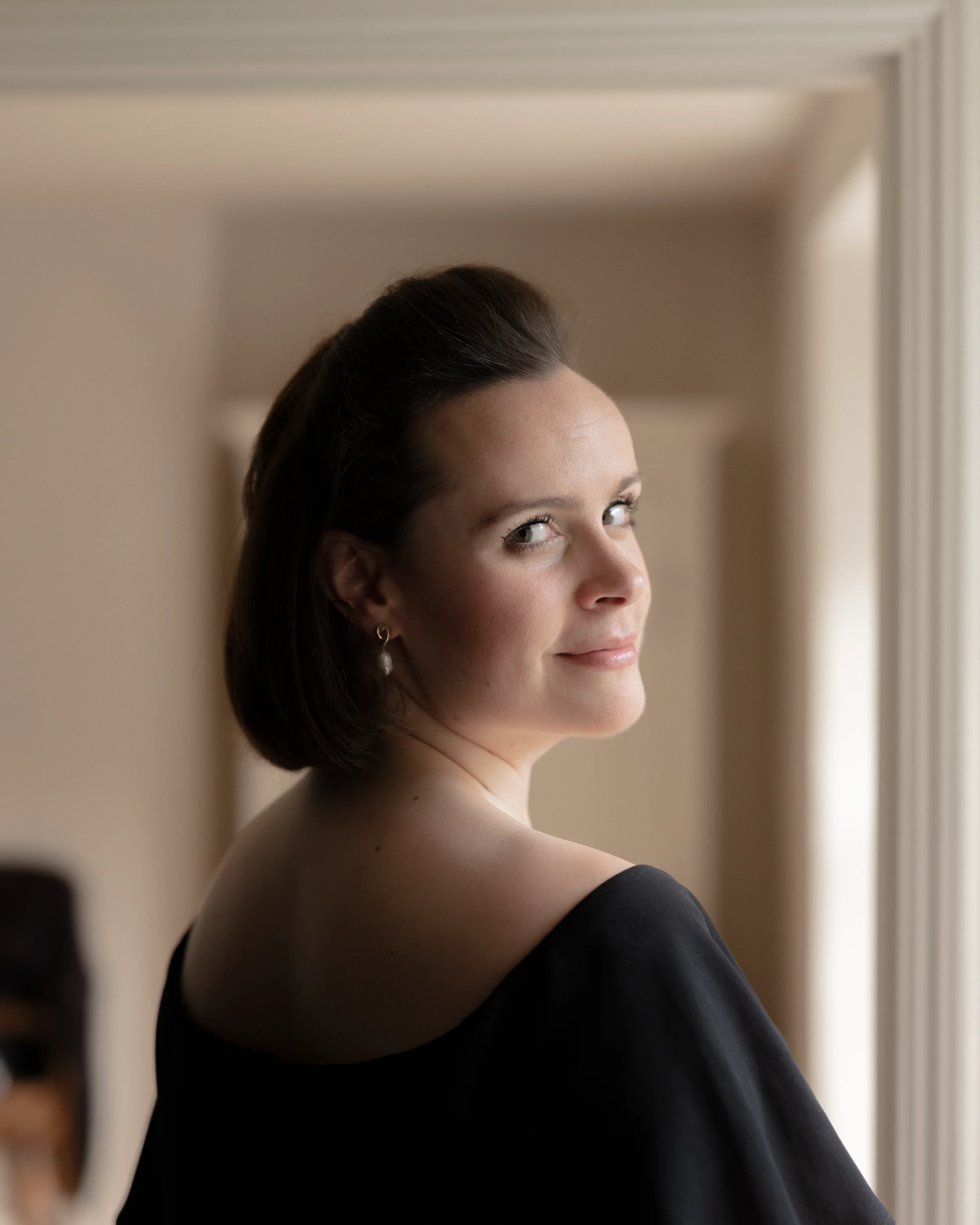Katy Thomson in black looking over her shoulder in a softly lit interior