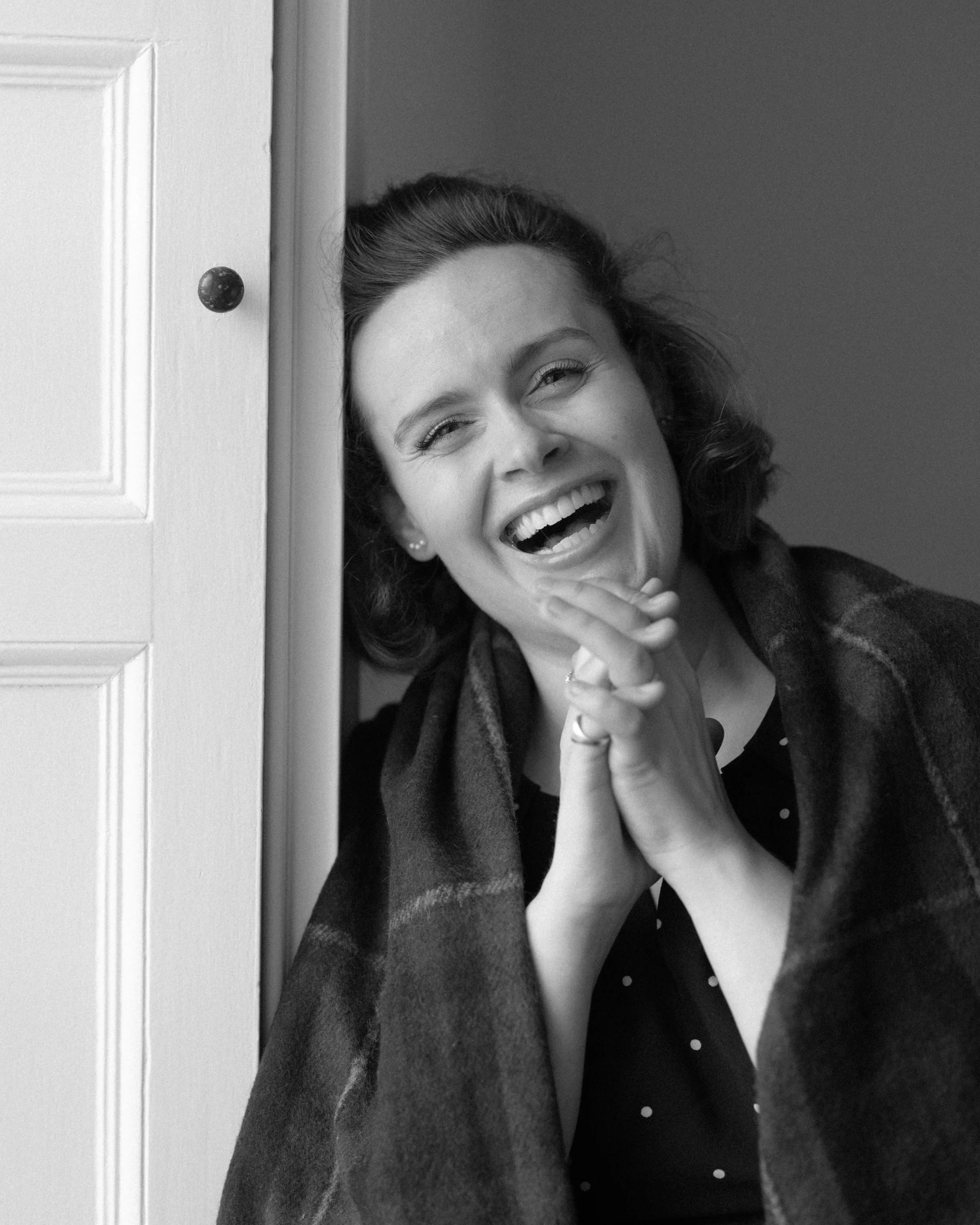 Black-and-white portrait of Katy Thomson smiling beside a doorway