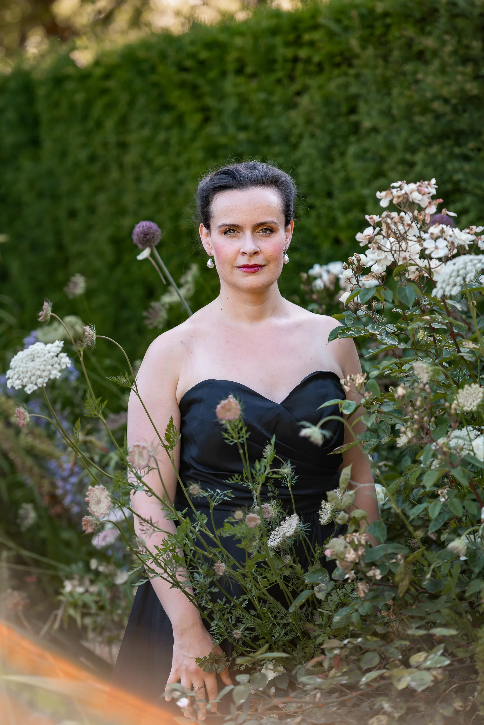 Katy Thomson in a black evening dress standing among garden flowers
