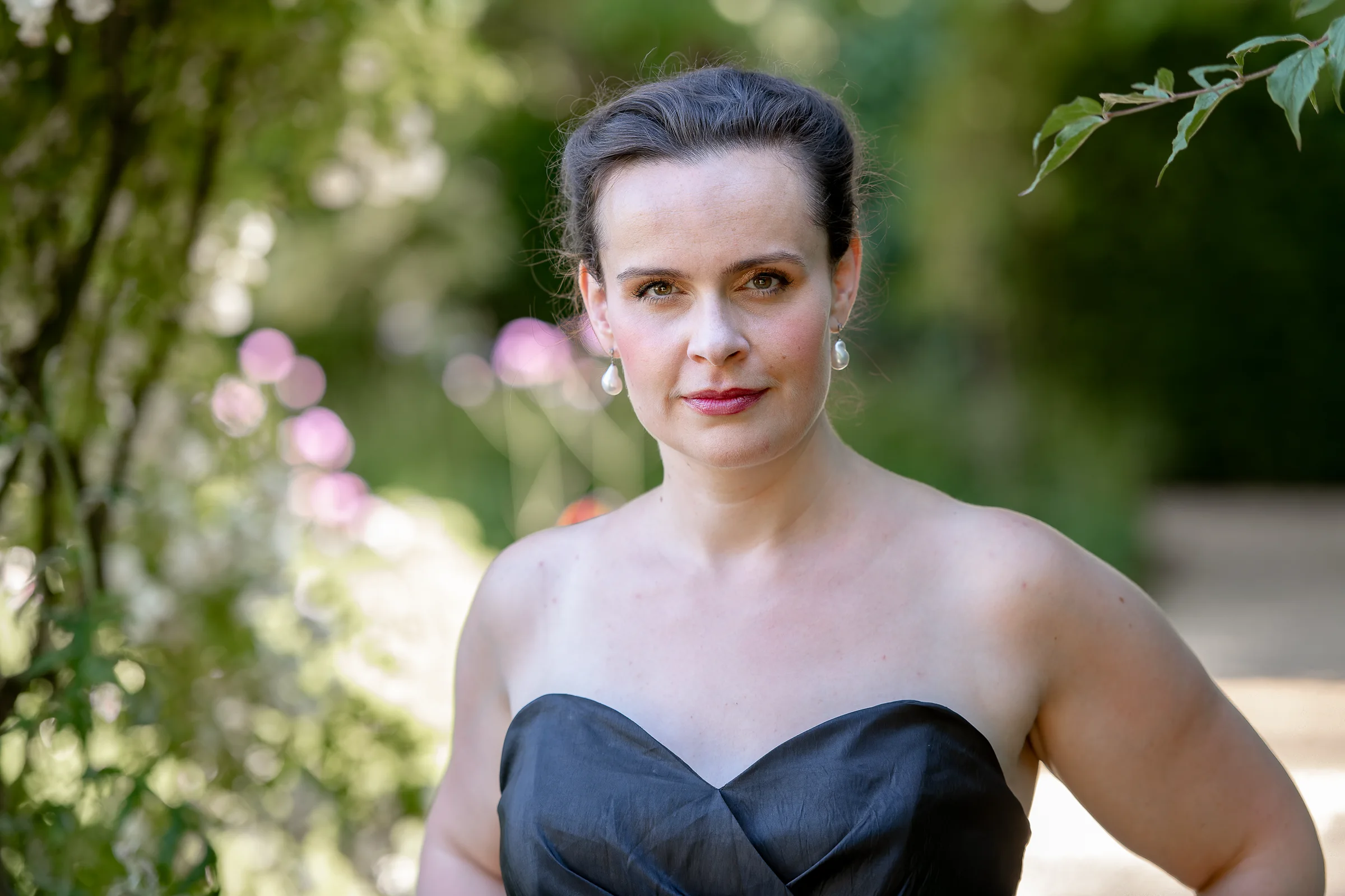 Katy Thomson in a black evening dress looking towards the camera in a garden